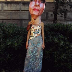 Tapestry bustier sequined sheer dress with one sleeve with a Big Head paper mask in Montjuic Barcelona