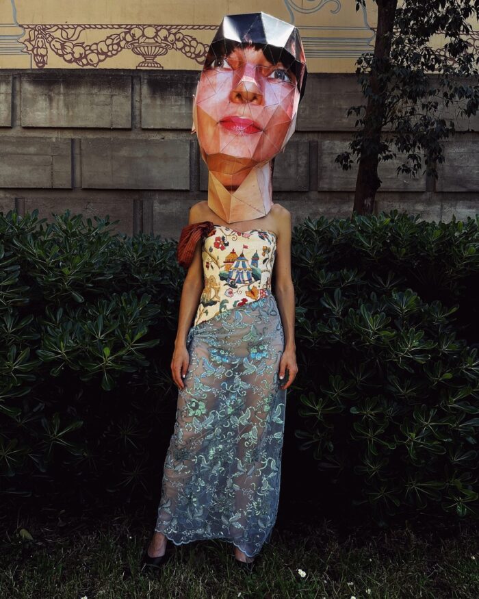 Tapestry bustier sequined sheer dress with one sleeve with a Big Head paper mask in Montjuic Barcelona